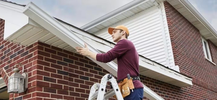 Installer fitting a new seamless gutter section on a brick home